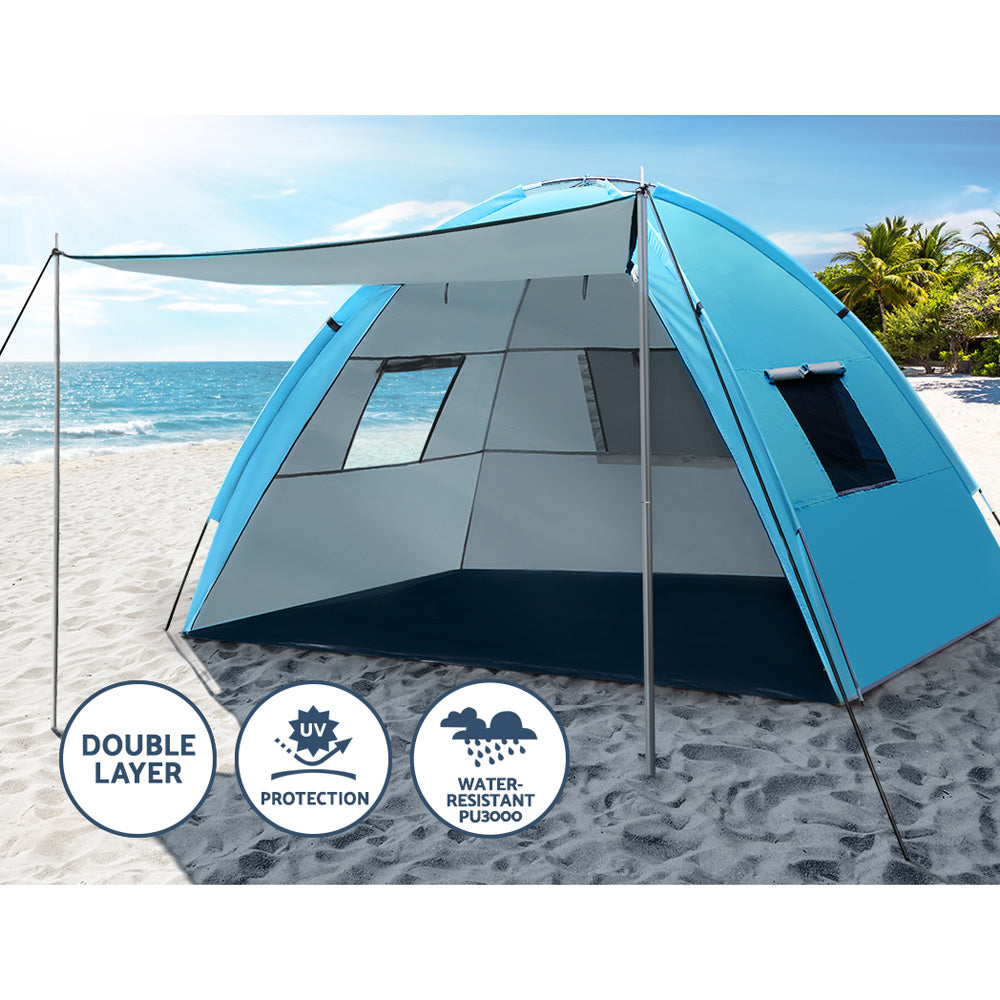 Blue and gray tent on a sandy beach with ocean and palm trees in the background
