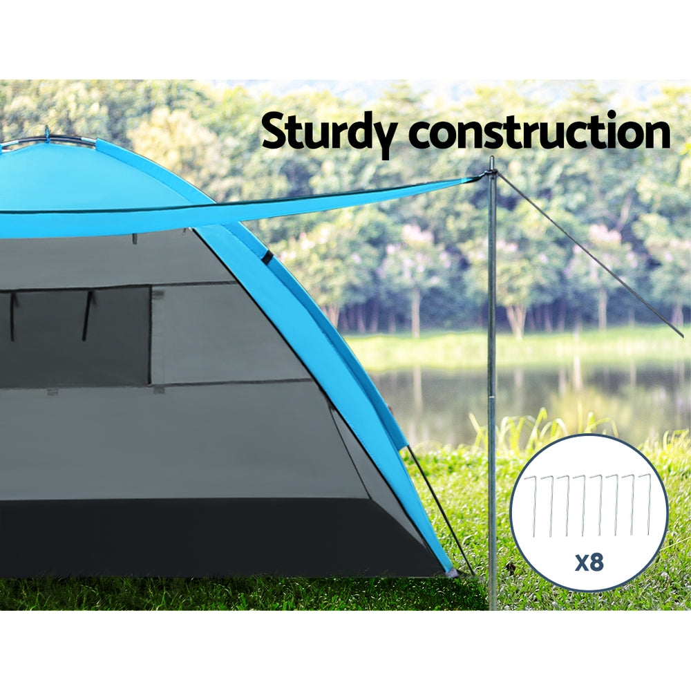 Camping tent with blue roof and gray sides, set up outdoors near a lake.